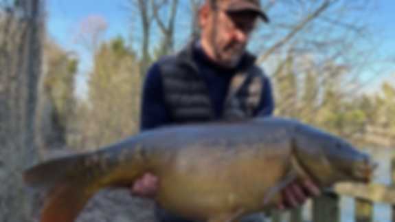 A fisherman poses with a fish he has caught. There is a bright blue sky visible.