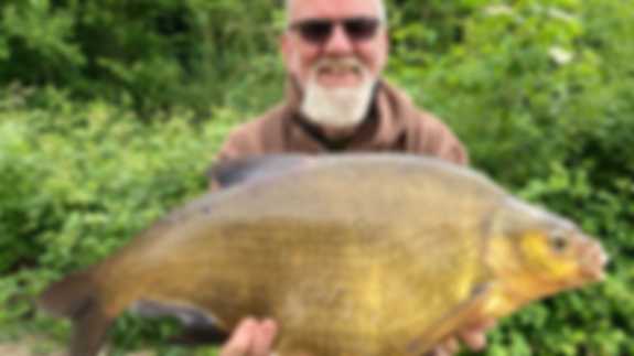 A fisherman poses with a Bream fish he has caught. He has a beard.