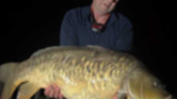 A fisherman poses with a Scaly Mirror fish he has caught.