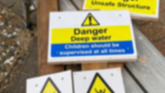 Warning Signs A photo of multiple brightly-coloured warning signs on the ground. They warn about deep water and slippery surfaces.
