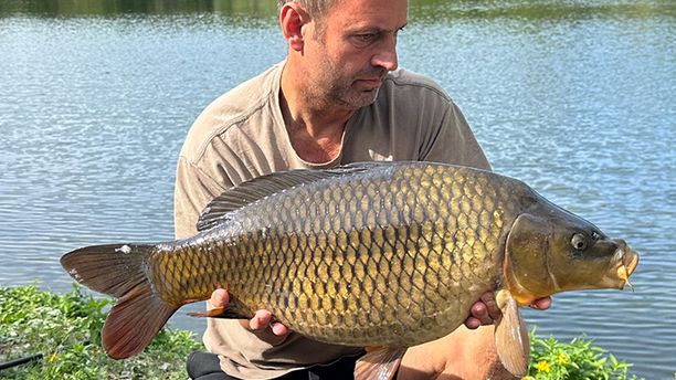 A person kneeling whilst holding a caught fish, with a lake in the background. It's a sunny day.