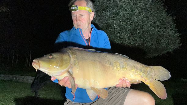 A Mirror fish caught by a fisherman in low-light conditions.