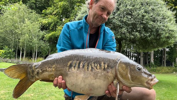 A Mirror fish caught by a smiling fisherman.